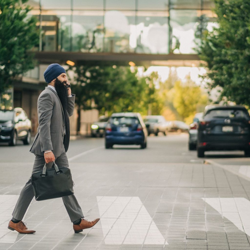 Sikh businessman with a turban crossing a city street on a zebra crossing, carrying a briefcase. — All-Round Contribution: Ge