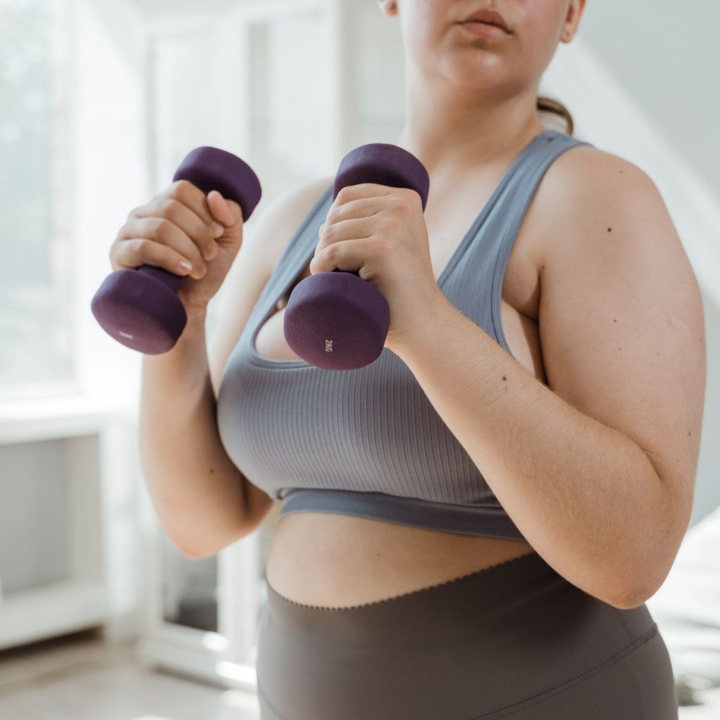 Plus size woman in activewear working out with dumbbells indoors, promoting body positivity. — Bad Breath After Gastric Sleev
