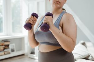 Plus size woman in activewear working out with dumbbells indoors, promoting body positivity. — Bad Breath After Gastric Sleev