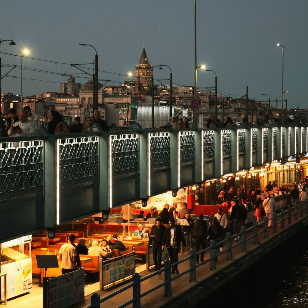 Night view of Galata Bridge bustling with people and distant Galata Tower in Istanbul. — Beyond Discomfort: Dr Vidal Sheen 's