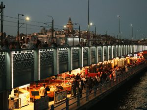 Night view of Galata Bridge bustling with people and distant Galata Tower in Istanbul. — Beyond Discomfort: Dr Vidal Sheen 's