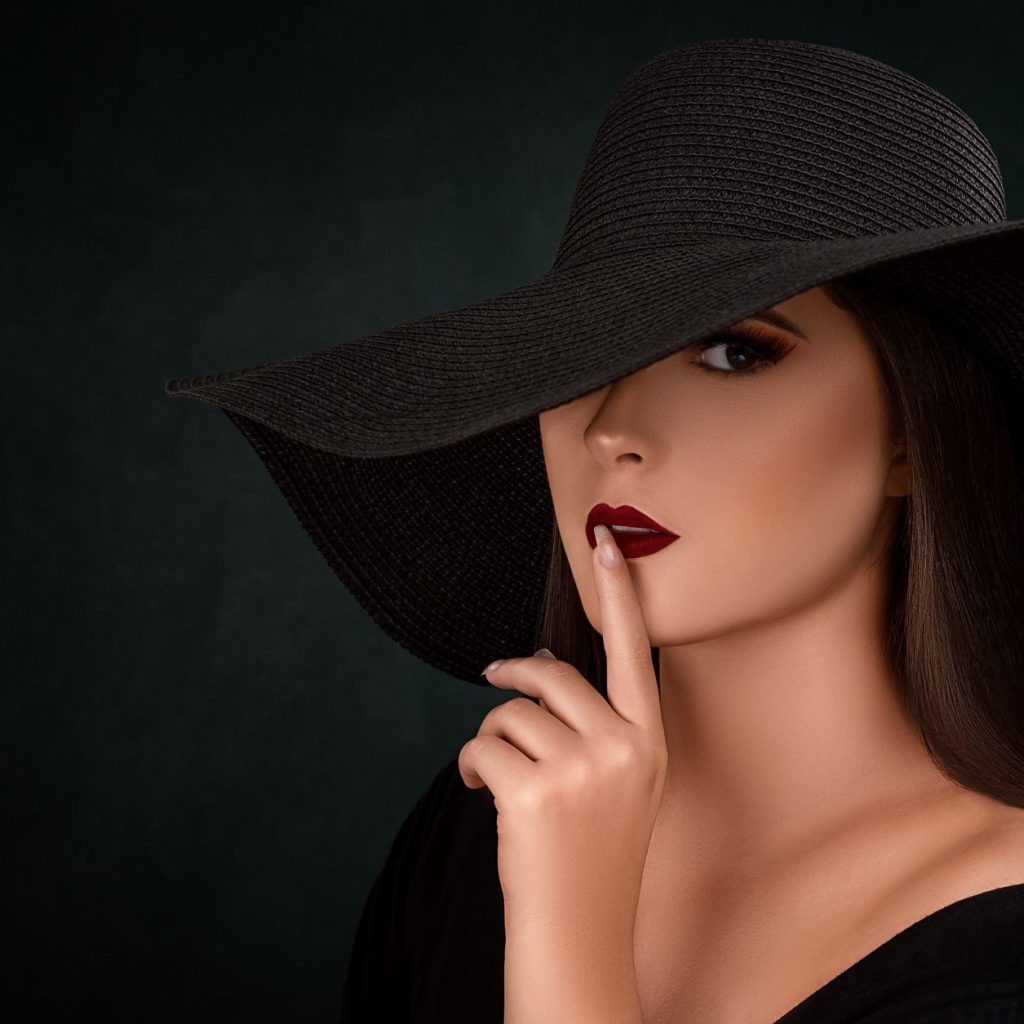 Mysterious woman in black hat making a hush gesture with dark background. — Body and Joint Pains No More
