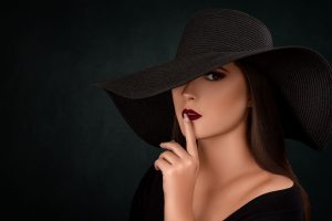 Mysterious woman in black hat making a hush gesture with dark background. — Body and Joint Pains No More