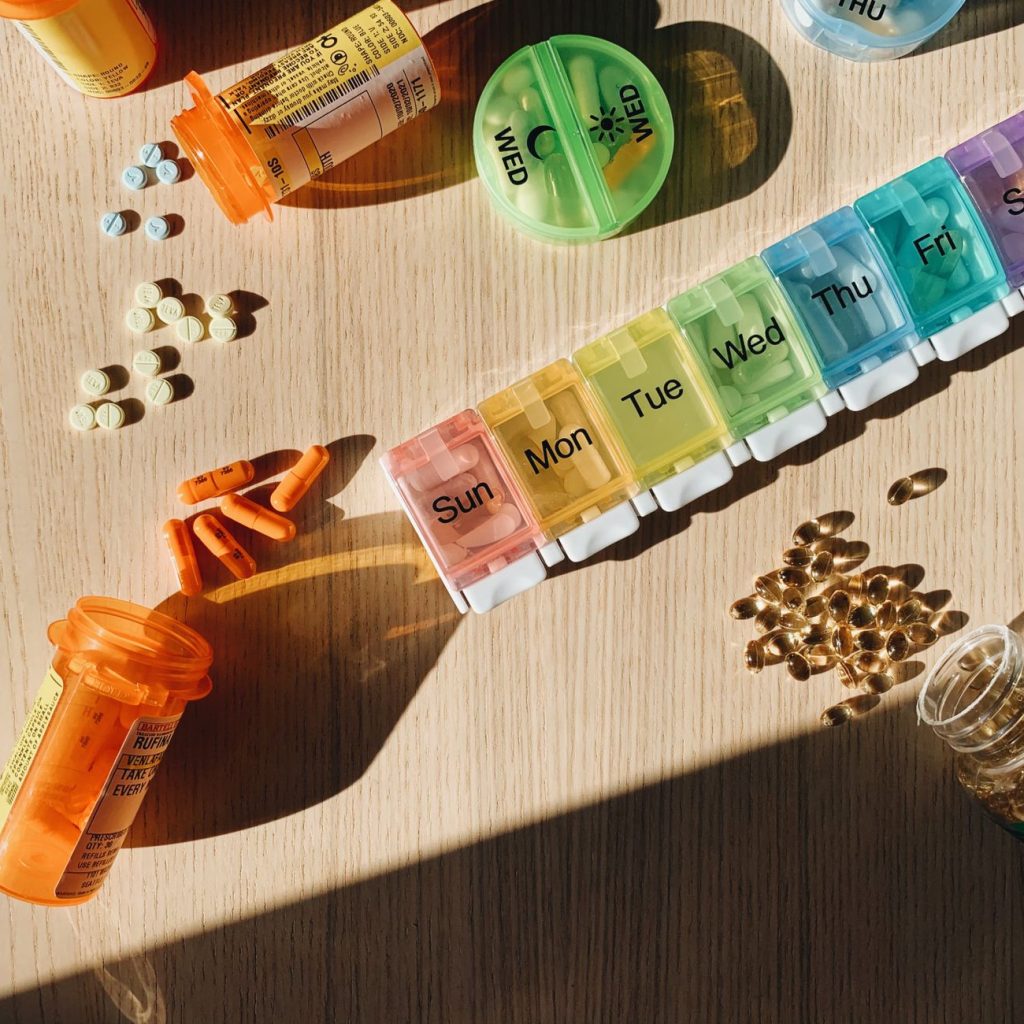 Colorful pill organizer with medication bottles and tablets on a wooden surface. — Canadian Immigration Medical Examination