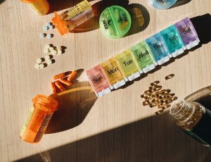 Colorful pill organizer with medication bottles and tablets on a wooden surface. — Canadian Immigration Medical Examination