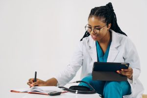 Smiling female doctor in scrubs using tablet and taking notes in a healthcare setting. — Essential Info on CBD Topicals