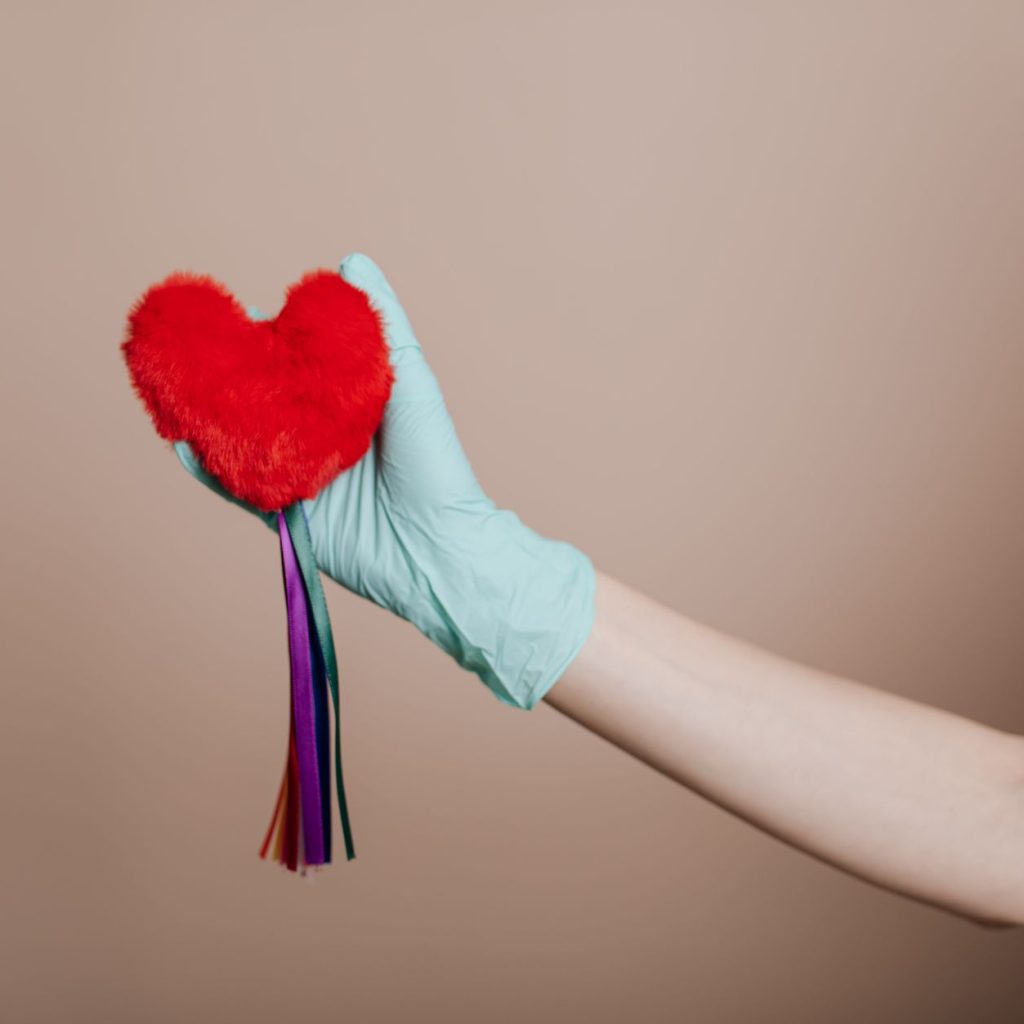 A latex-gloved hand holds a red heart-shaped plush with colorful strings, symbolizing love and safety. — Everything You Need