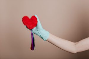 A latex-gloved hand holds a red heart-shaped plush with colorful strings, symbolizing love and safety. — Everything You Need