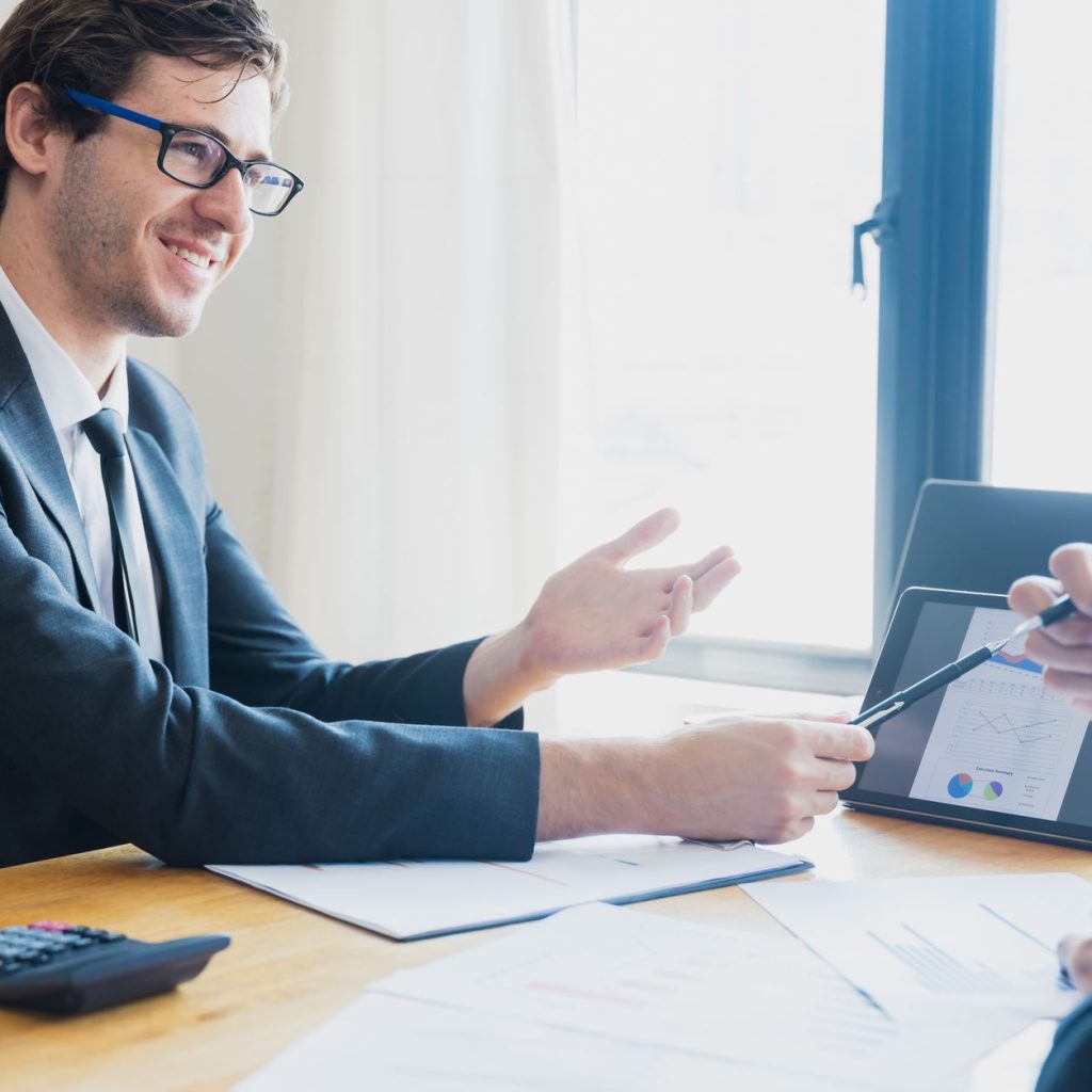 Two businessmen in formal attire discussing a business report in an office setting with a tablet. — Exploring Plastic Surgery