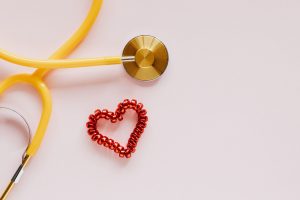 From above of yellow stethoscope near small red bead heart made for San Valentines Day on pale pink surface — Finer Methods f