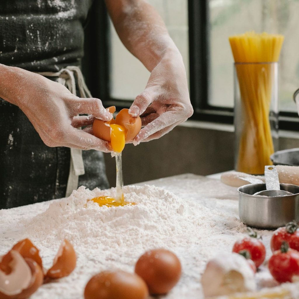 Crop anonymous person adding egg in flour while cooking pastry for recipe with cherry tomatoes and spaghetti — Food Allergies