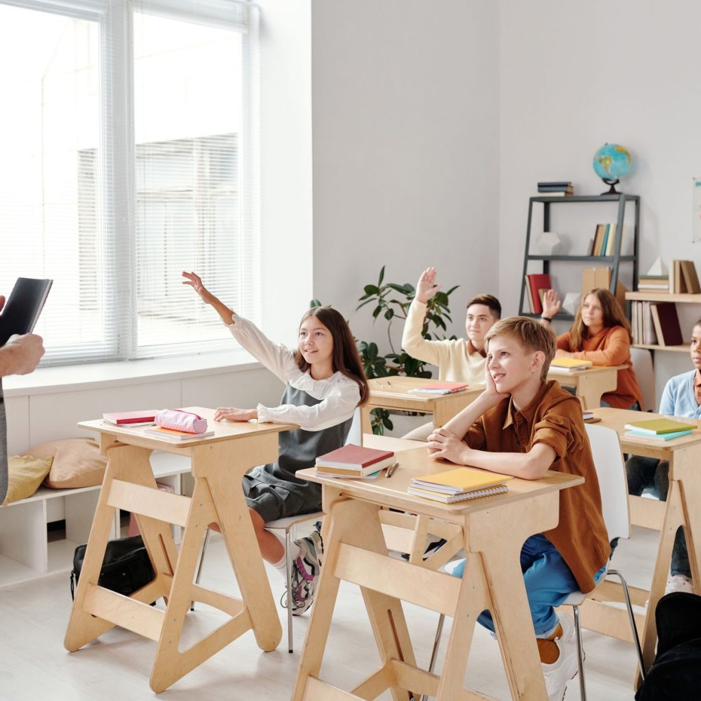 Students engage eagerly in a classroom, raising hands and participating in a lesson with their teacher. — Gap Year Volunteer