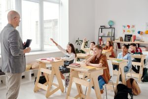 Students engage eagerly in a classroom, raising hands and participating in a lesson with their teacher. — Gap Year Volunteer