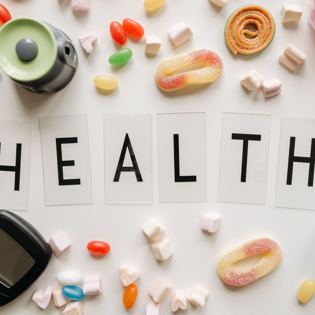 Creative flat lay with sweets around a 'HEALTH' text and monitoring device, symbolizing diabetes awareness. — Great of London