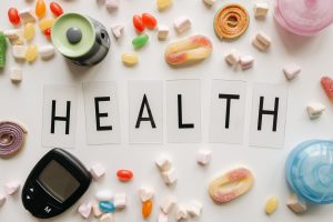 Creative flat lay with sweets around a 'HEALTH' text and monitoring device, symbolizing diabetes awareness. — Great of London