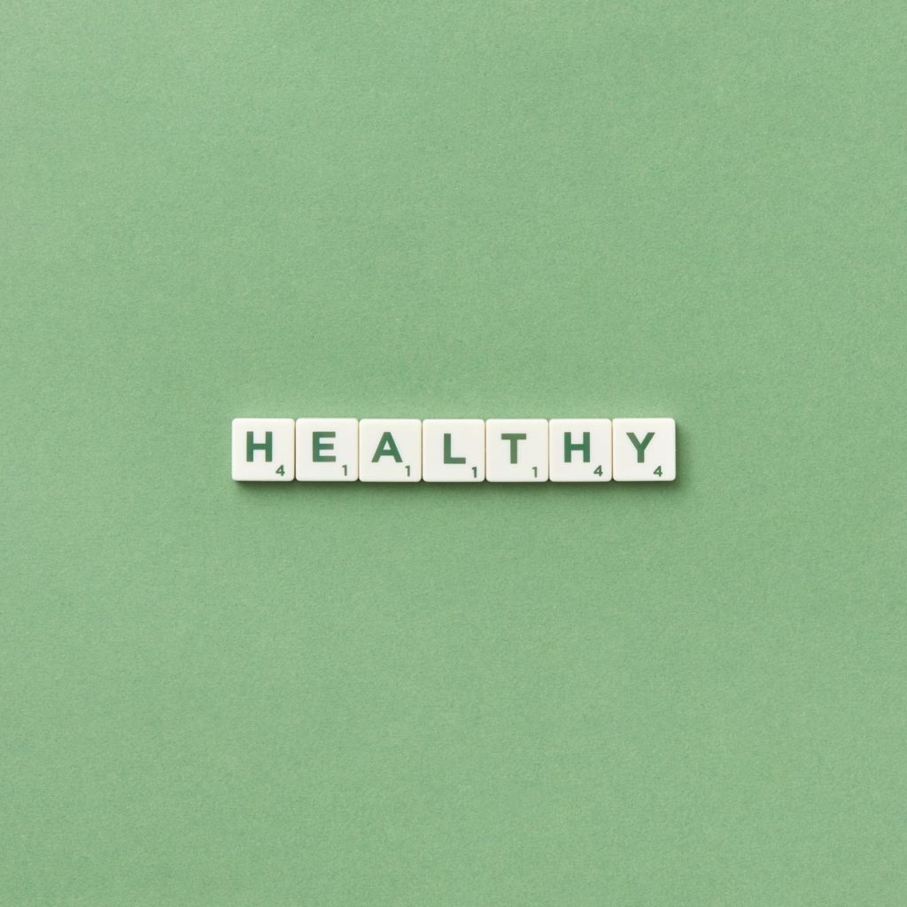 Scrabble tiles spelling the word 'healthy' on a light green background, top view. — Health Benefits of NAD Injections