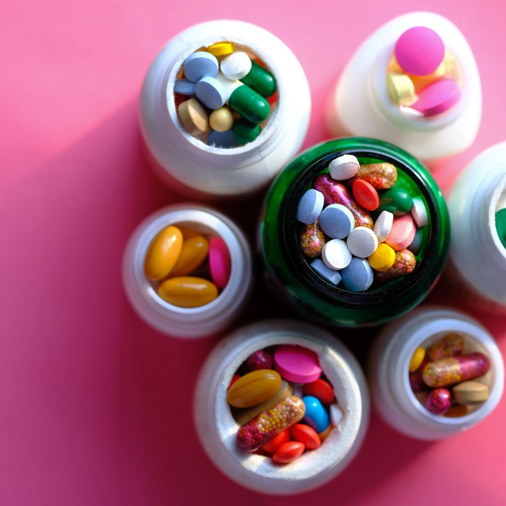 Top view of various medication pills and capsules in containers with bright pink backdrop. — Health Care Review
