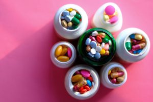 Top view of various medication pills and capsules in containers with bright pink backdrop. — Health Care Review