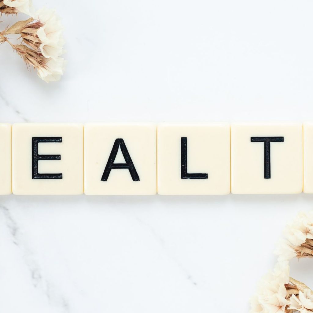 Creative arrangement of scrabble tiles spelling 'Health' with white flowers on a marble surface. — Healthier SG: Transforming