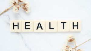Creative arrangement of scrabble tiles spelling 'Health' with white flowers on a marble surface. — Healthier SG: Transforming