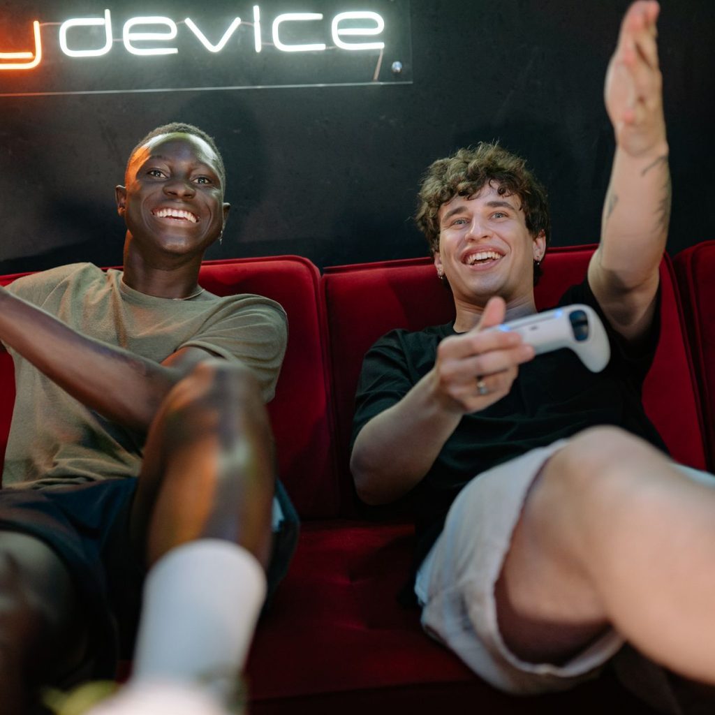 Two friends having fun and playing video games on a couch indoors. — How can I tell if an online casino is legit?