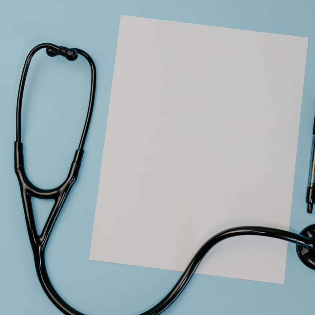 Flat lay of a stethoscope, blank paper, and pen on a blue background. — Juul Vs Myle: Which Vaping Device is Better?