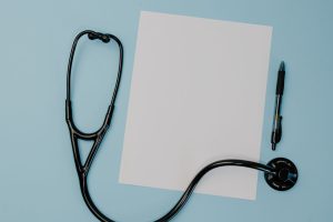 Flat lay of a stethoscope, blank paper, and pen on a blue background. — Juul Vs Myle: Which Vaping Device is Better?