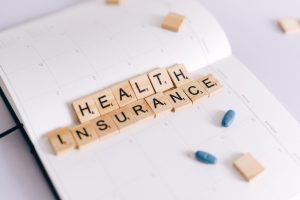 Close-up of health insurance spelled out with Scrabble tiles on a planner, alongside medication pills. — Medicare Advantage P