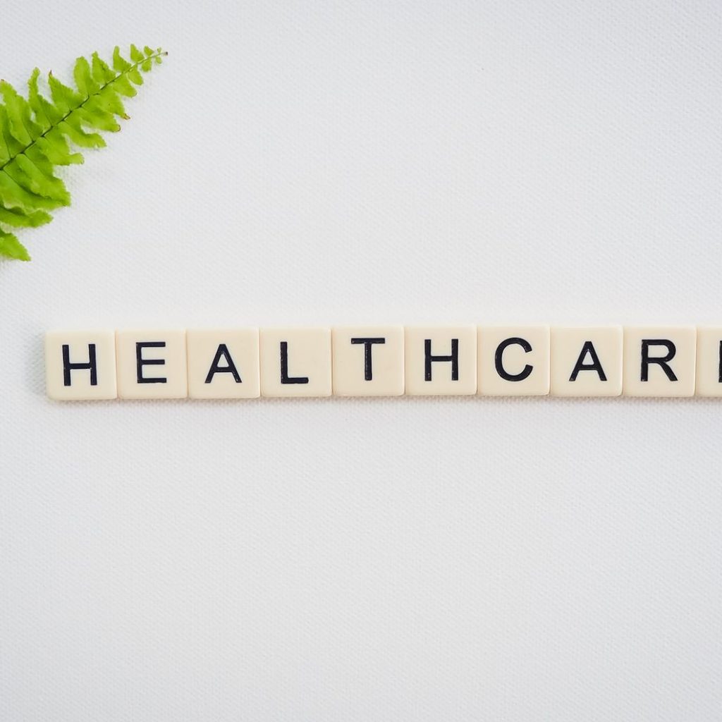 Healthcare word spelled with Scrabble tiles next to a green fern leaf on a white background. — Probiotics and Their Health Be