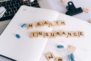 Scrabble tiles spelling 'Health Insurance' on planner with pills and laptop, symbolizing healthcare planning. — Seven Princip