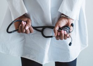 A medical professional holding a stethoscope in a clinical setting. — Stand Up And Glo!