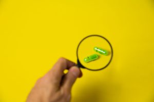From above of crop unrecognizable male holding magnifying glass over green pills on yellow background in studio — Why