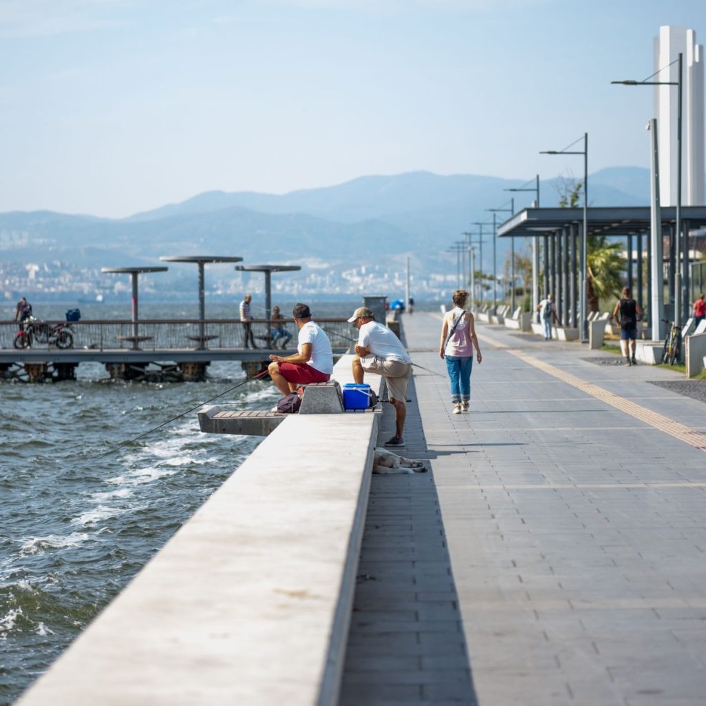 Serene seaside promenade with people fishing and strolling by the pier, set against coastal views. — The Basics of Online Rou