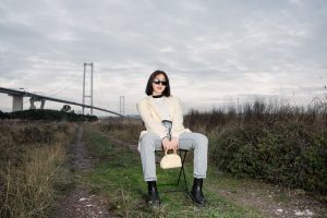 Stylish woman in sunglasses sitting by a bridge, showcasing modern fashion against a natural backdrop. — Things You Need to K