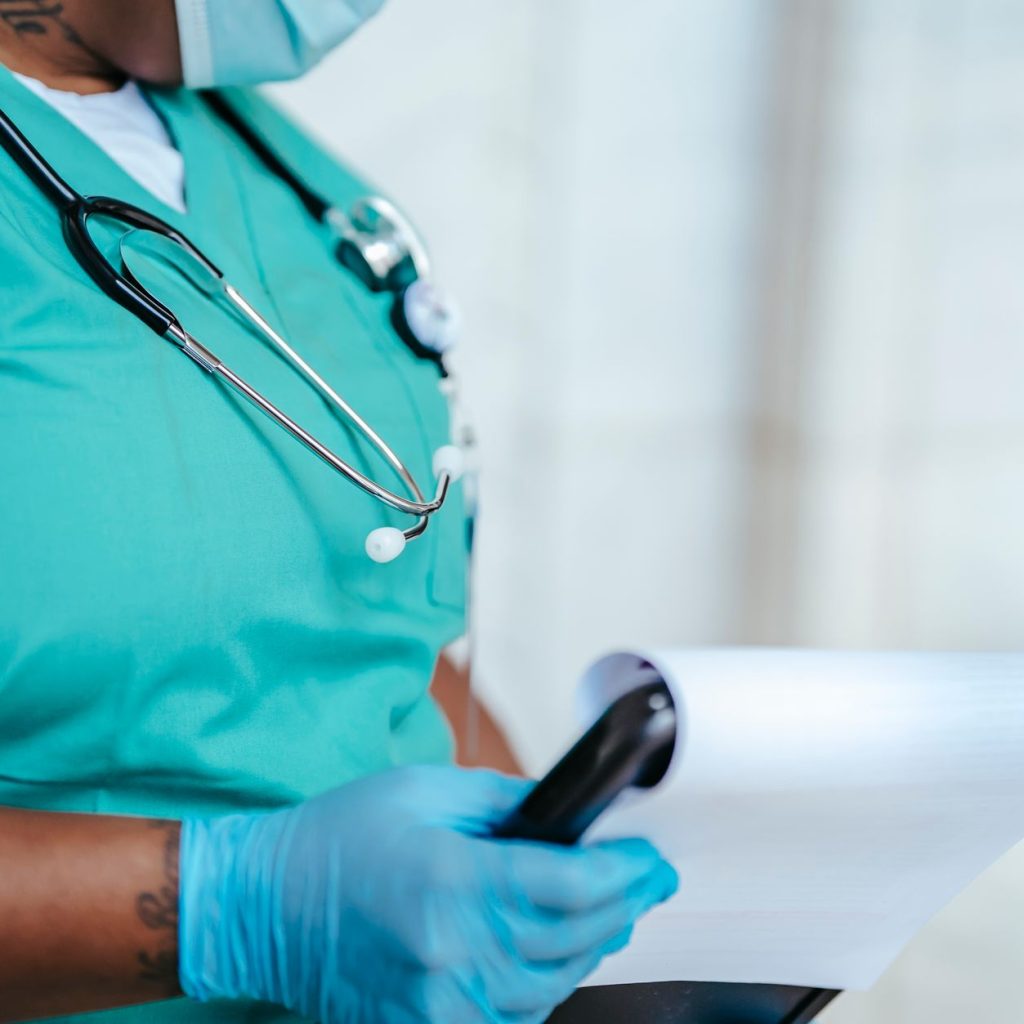Side view of crop anonymous tattooed ethnic female medic in uniform with stethoscope and papers on clipboard — Tips for buyin