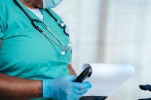 Side view of crop anonymous tattooed ethnic female medic in uniform with stethoscope and papers on clipboard — Tips for buyin
