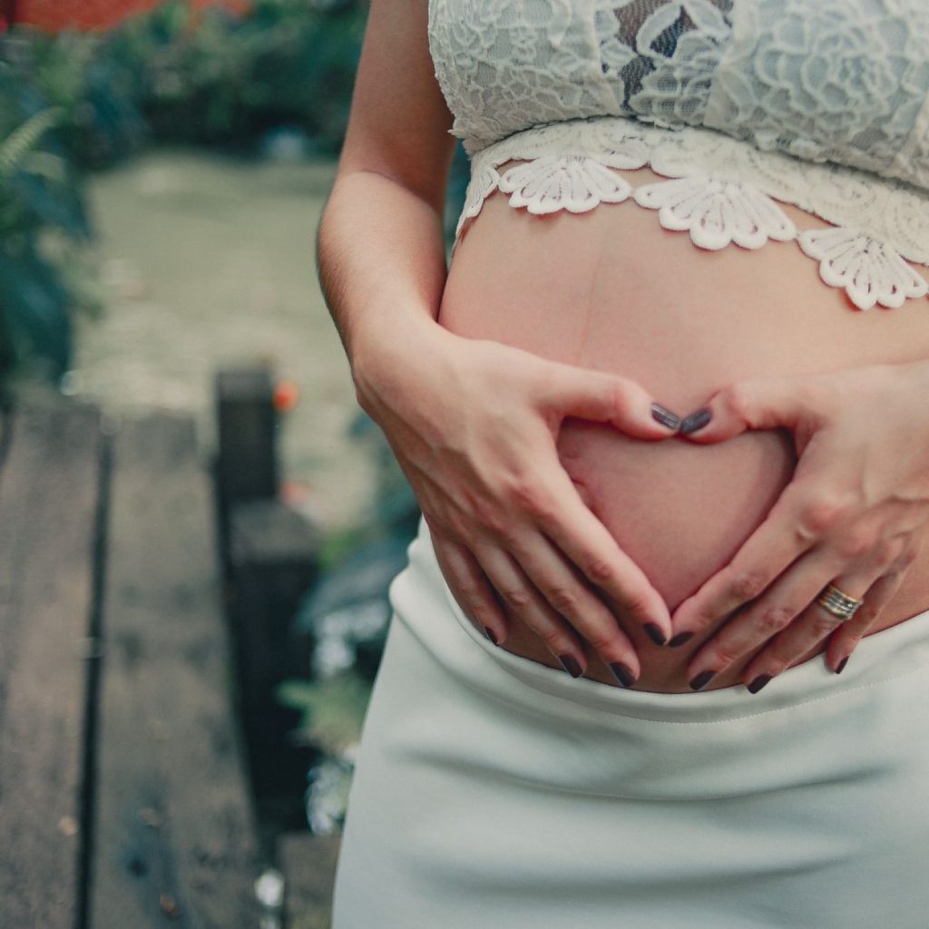 A pregnant woman making a heart shape on her baby bump in an outdoor setting. — Top 3 Foods That Can Help Deal with Pregnancy