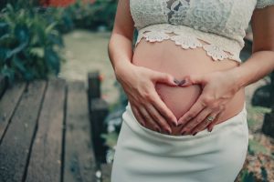A pregnant woman making a heart shape on her baby bump in an outdoor setting. — Top 3 Foods That Can Help Deal with Pregnancy
