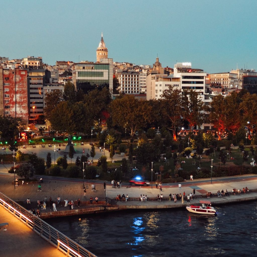 Scenic view of Istanbul's skyline featuring Galata Tower and bustling park at twilight along the waterfront. — What Are the M