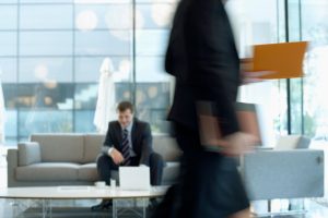 Businessman sitting in modern office lounge using a laptop while colleague walks past, creating dynamic blur. — What is an Ev