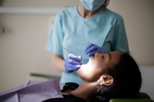 Focused female dentist in mask uniform and latex gloves using instruments for examining teeth of African American lady while