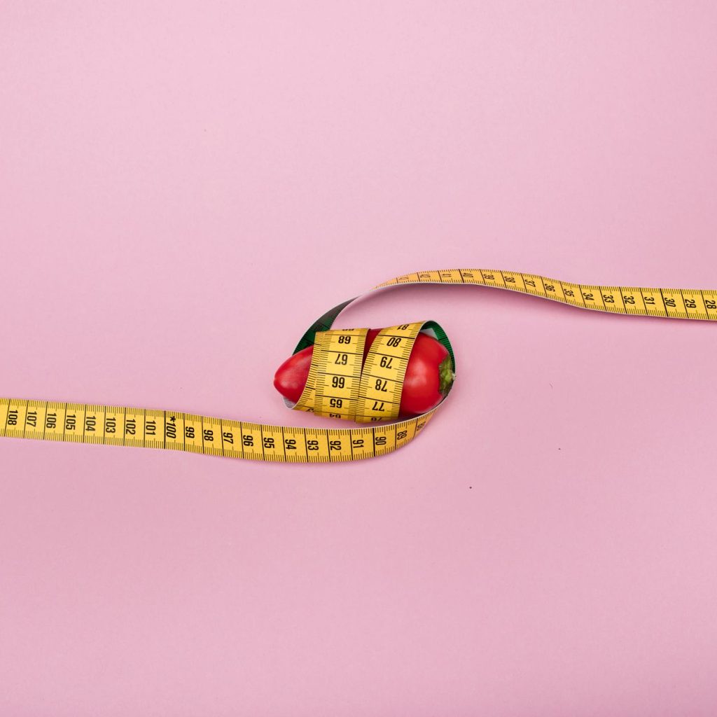 A red bell pepper wrapped with a yellow measuring tape on a pink background symbolizing diet and health. — What Is The Paleo