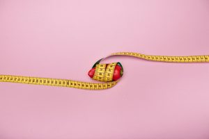 A red bell pepper wrapped with a yellow measuring tape on a pink background symbolizing diet and health. — What Is The Paleo