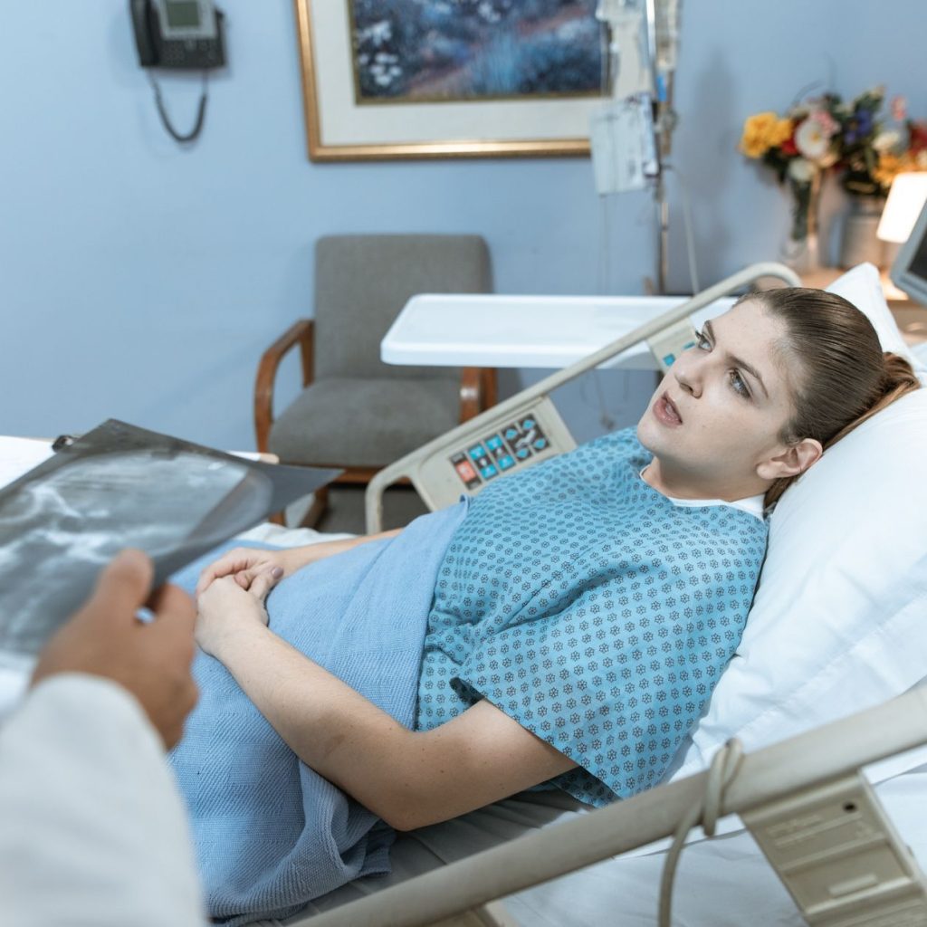 Caucasian woman in hospital bed receiving care from healthcare professional. — Where To Find Pregnancy Help