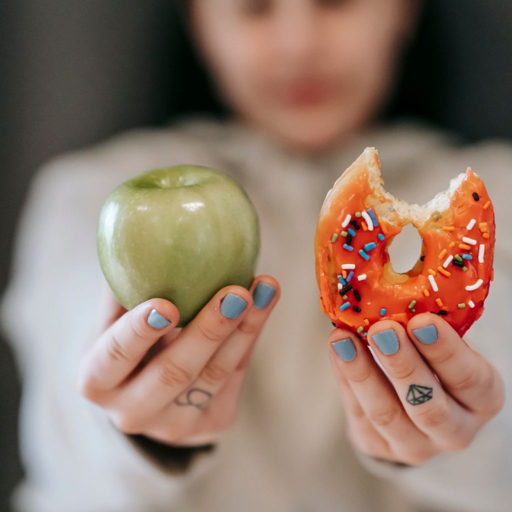 Crop anonymous female demonstrating delicious sweet donut and fresh green apple while making decision — Why do fitness expert