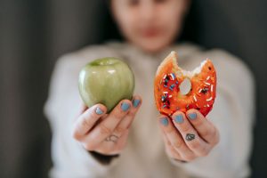 Crop anonymous female demonstrating delicious sweet donut and fresh green apple while making decision — Why do fitness expert