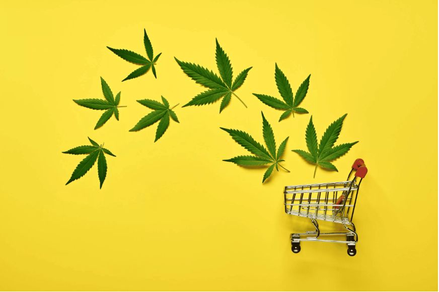 A small shopping cart beside several cannabis leaves on a bright yellow background.